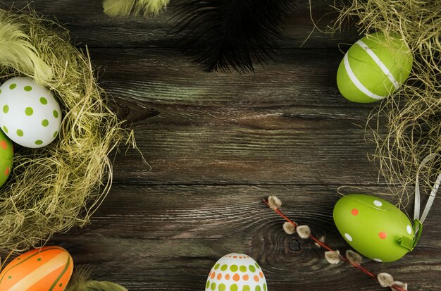 Green and orange Easter eggs in a sisal nest on an old wooden background. Bird feathers. Painted eggs