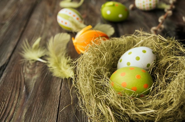 Green and orange easter eggs in a sisal nest on a wooden surface copy space. Painted eggs. Bird feathers.