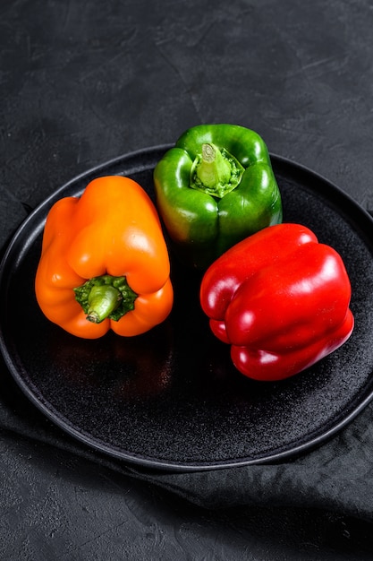 Green, orange and red bell peppers on a black plate. Top view.