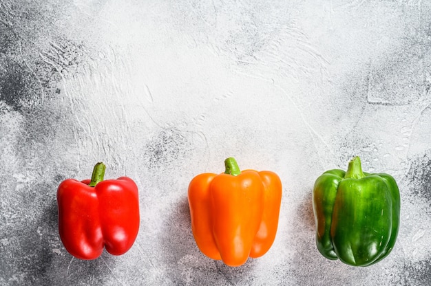 Green, orange and red bell peppers. Gray background. Top view. Space for text.