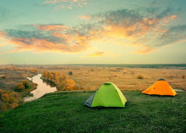 Green and orange tent on riverbank on sunny summer day