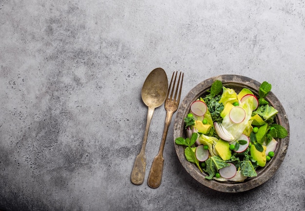 Green organic vegetables salad with avocado, kale, sprouting herbs in rustic bowl on gray concrete background, close-up, top view. Healthy clean eating, diet or detox concept with space for text