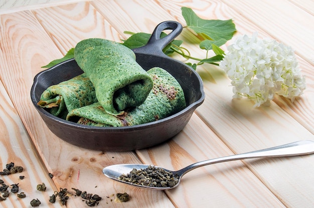 緑茶を加えた生地からの緑のパンケーキ明るい木製の背景に鋳鉄製の鍋で食事療法食品健康食品