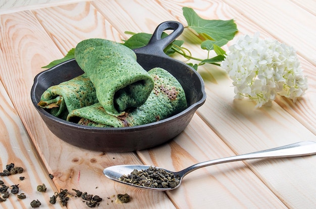 Green pancakes from dough with the addition of green tea In a cast iron pan on a light wooden background Dietary food Healthy food