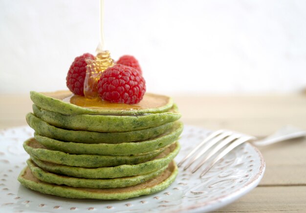 Green pancakes with honey and raspberries. on a light background.