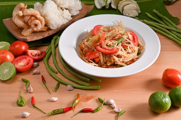 Green papaya salad and ingredients on wooden background. Thai food concept.