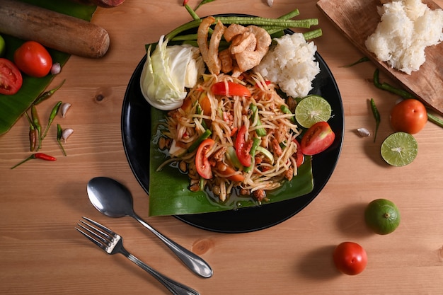 Green papaya salad with sticky rice on wooden table. Thai traditional food.