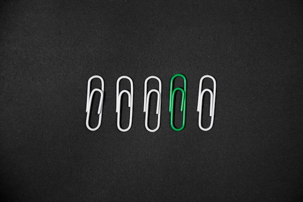 Green paper clip in the middle of white clips row unique idea\
concept isolated on black background