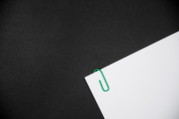 Green paper clip with white paperwork and reports arranged on black table Space for your text