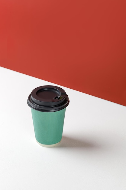 Зеленый бумажный стаканчик с кофе на белом фоне и красной стеной Одноразовый макет бумажного стаканчика