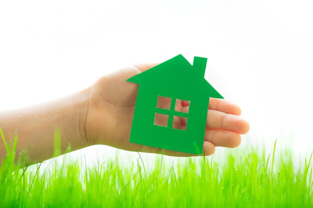 Дом из зеленой бумаги в руке над весенней травой