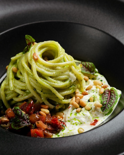 green pasta spaghetti with pesto sauce, tomatoes and basil. pasta with spinach vegetables and nuts