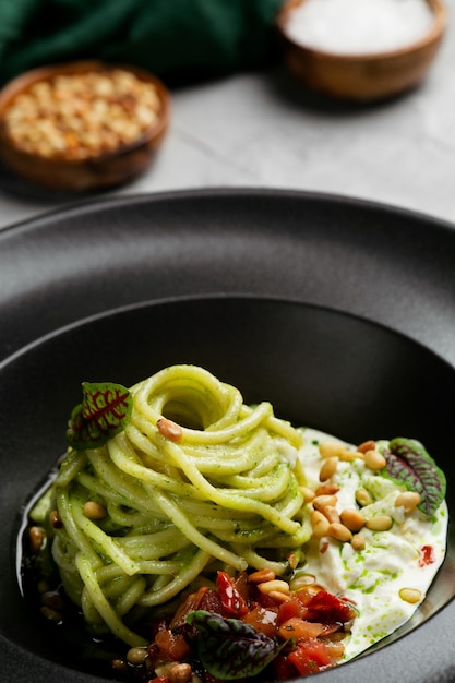 green pasta spaghetti with pesto sauce, tomatoes and basil. pasta with spinach vegetables and nuts