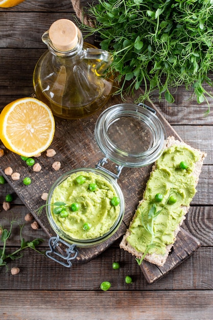 Green pea hummus fresh greens vegetables crackers served on a wooden board top view