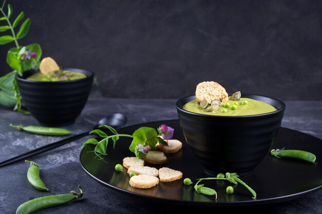 Green peas cream soup with croutons in a black bowl