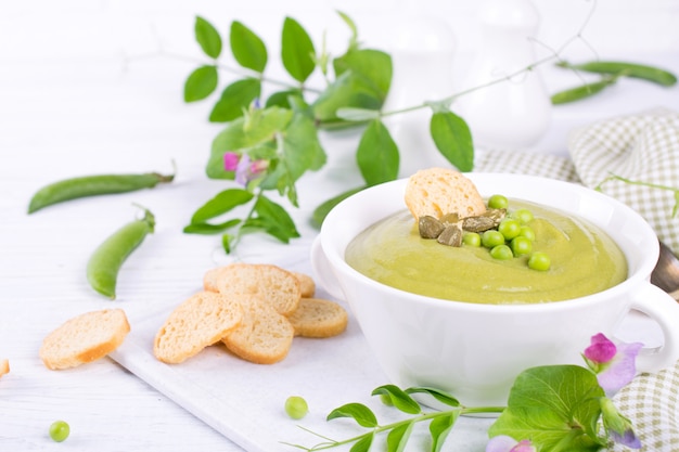 Green peas cream soup with croutons in a white bowl