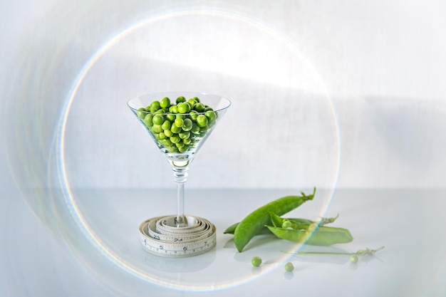 Foto piselli verdi in un bicchiere su fondo di legno bianco con nastro adesivo di misurazione concetto di alimentazione sana