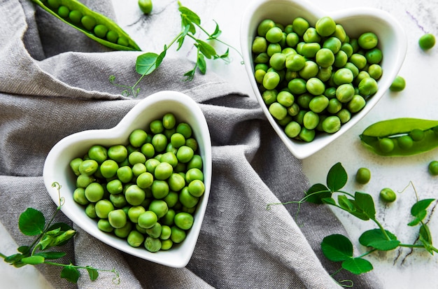 Green peas in heart shaped bowls on a fabric surface