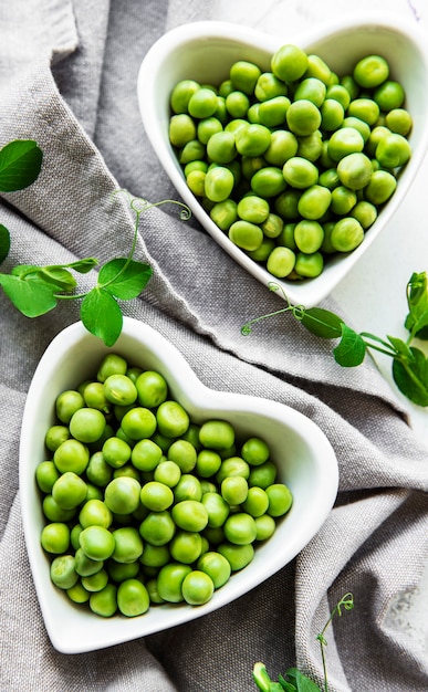 Green peas in heart shaped bowls on a fabric surface