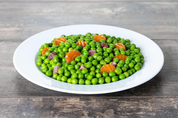 Green peas with serrano ham and carrot on wooden table