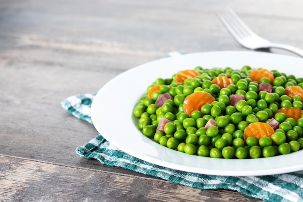 Green peas with serrano ham and carrot on wooden table