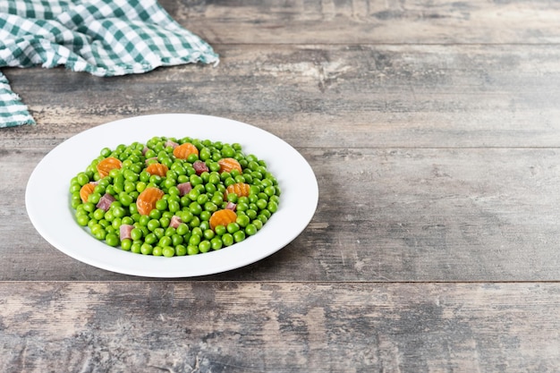 Green peas with serrano ham and carrot on wooden table