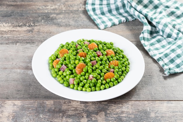 Green peas with serrano ham and carrot on wooden table