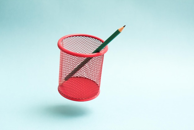 Green pencil in a flying pink cup on blue background