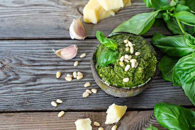 Green pesto in a bowl made from fresh basil leaves pine nuts parmesan garlic and olive olia on wooden background