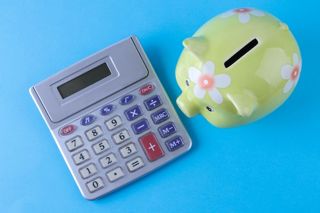 明るい青色の背景に緑の豚の貯金箱と電卓。財政、貯蓄、お金。上面図