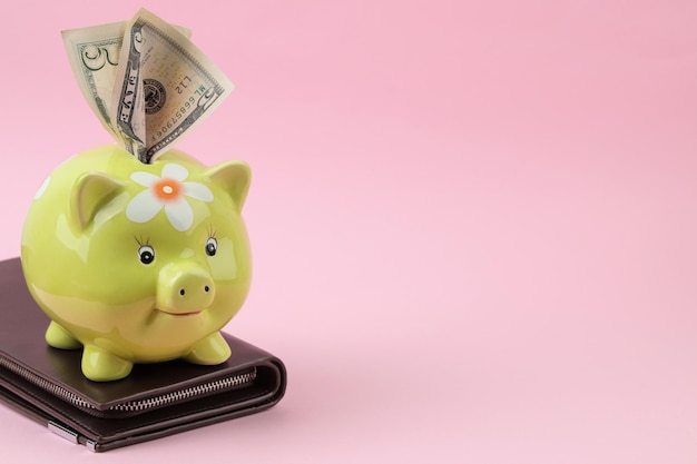 緑の豚の貯金箱と財布と明るいピンクの背景にお金。財政、貯蓄、お金。テキストの場所。