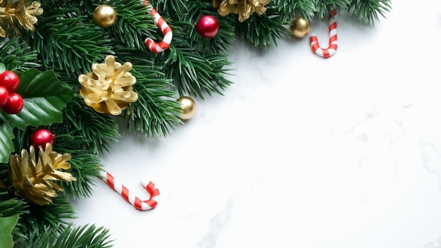 Зеленые листья сосны, красные рождественские украшения и леденцы на белом мраморном фоне, рождественские украшения ярко-красного цвета. Простая и креативная рождественская концепция.