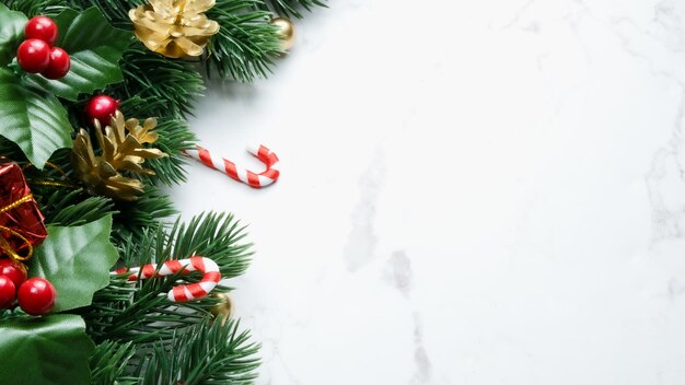 Green pine tree leaves, red christmas decorations and candy
canes on white marble background, christmas decorations in bright
red color. simple and creative christmas concept.