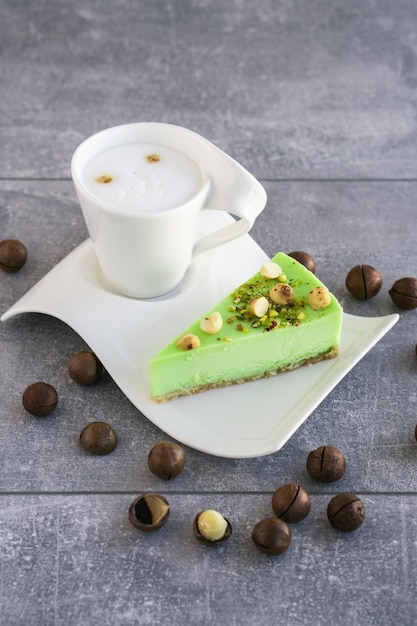 Green pistachio cake with macadamia nuts on white plate with cappuccino Creamy pistachio cheesecake