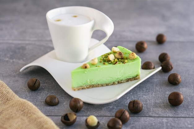 Green pistachio cake with macadamia nuts on white plate with cappuccino Creamy pistachio cheesecake