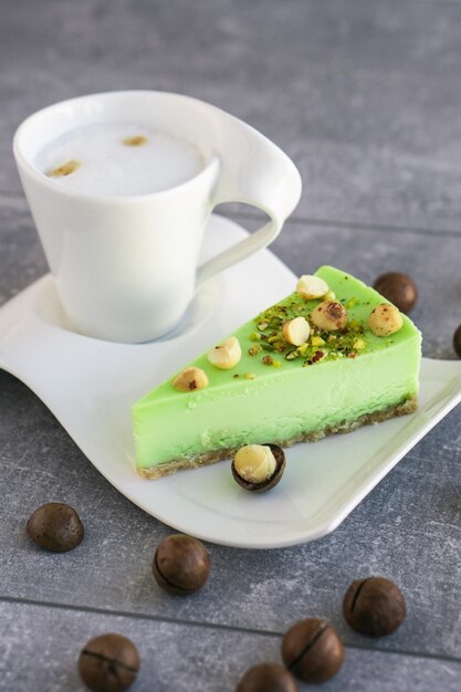 Green pistachio cake with macadamia nuts on white plate with cappuccino Creamy pistachio cheesecake