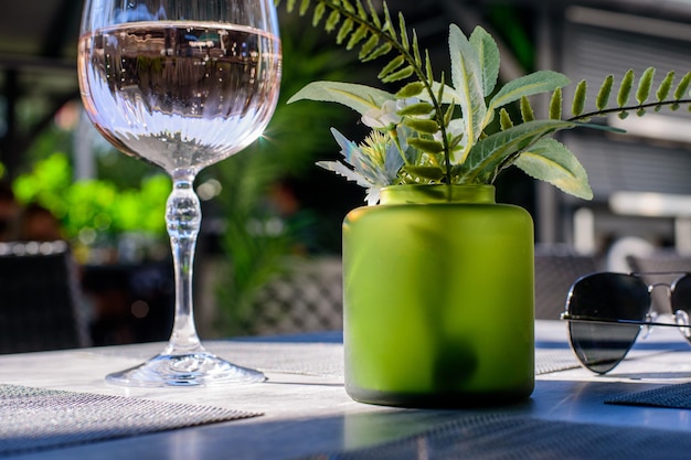 green plants in glass green vase and glass of rose wine on gray background