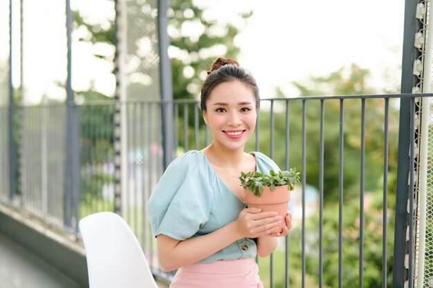 발코니에 아름 다운 행복 한 아시아 여자 손에 냄비에 녹색 식물