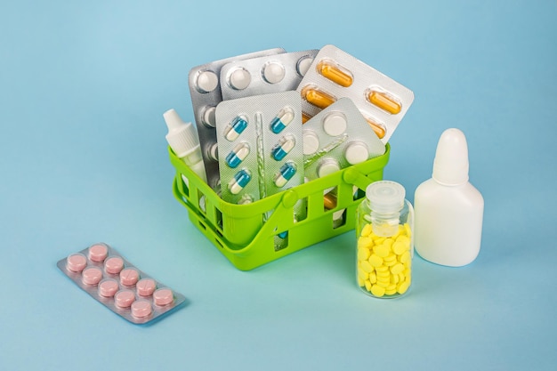 A green plastic basket with pills and a bottle of pills on a blue background.