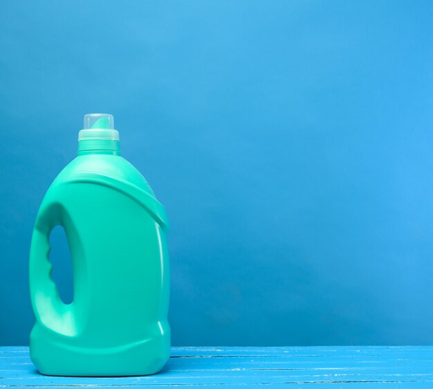 Green plastic bottle with detergents on blue background, copy space