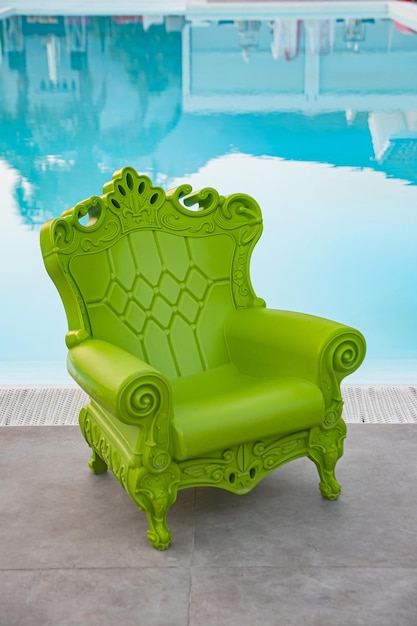 青いプールの端に彫刻が施されたベクトリアン様式の緑色のプラスチック製の椅子