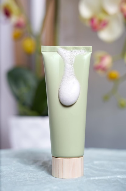 Green plastic tube with organic cosmetics, hand, face, body cleansing foam on a floral view. Eco-friendly cosmetics