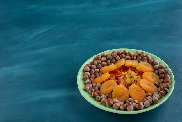 Piatto verde di frutta secca e nocciole sul tavolo blu.