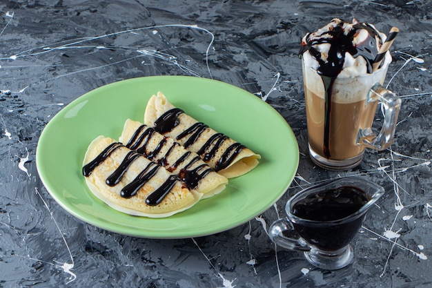 Green plate of homemade crepes with chocolate topping and glass of iced coffee. 