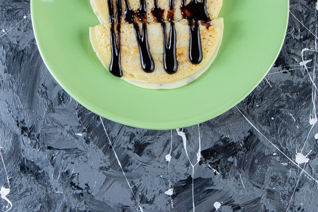 Green plate of homemade crepes with chocolate topping on marble surface.