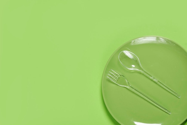 Зеленая тарелка и пластиковая вилка с ложкой на зеленом фоне копией пространства