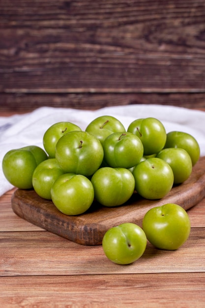 Green plum on wood background Pile of green plums on wooden serving plate close up