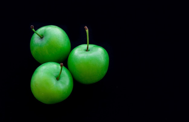 Green plums isolated on black background. Top view photo of green plum fruits with space for text.