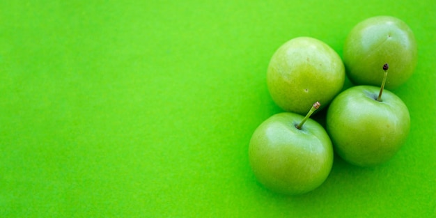 Green plums isolated on green background. Top view photo of sour plum fruits with space for text.