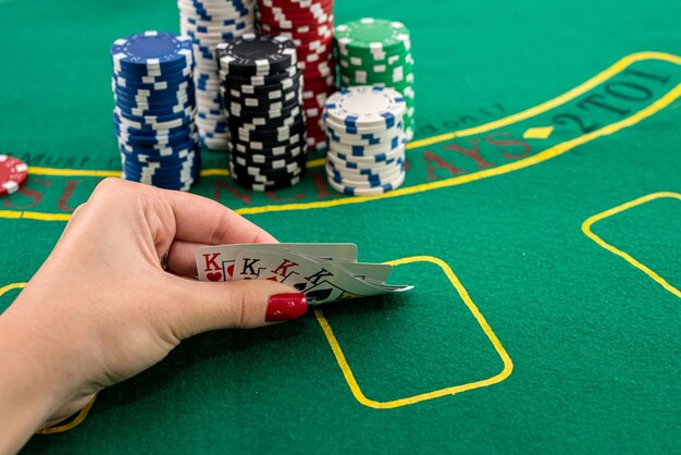 on a green poker table there are colored chips on top of each other and a female hand is holding cards. Poker concept